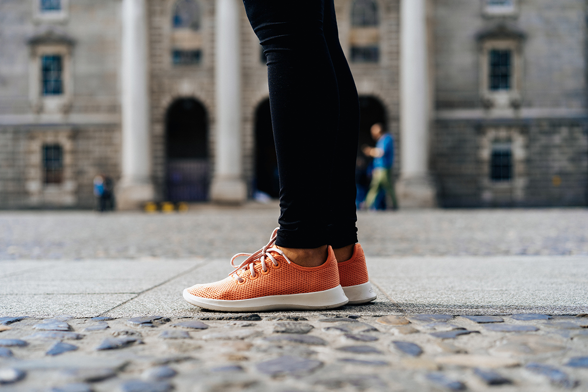 A person wearing orange shoes standing on the ground. Photo by Dan Gold on Unsplash.